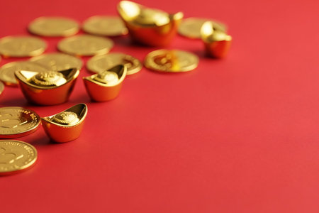 Gold coins and small ingots scattered on a vibrant red background creating a clean template ideal for commercial promotion of wealth.の素材