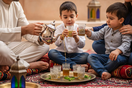 Family members sitting on cushions sharing freshly poured mint tea and enjoying quality time during Eid celebration gathering.の素材