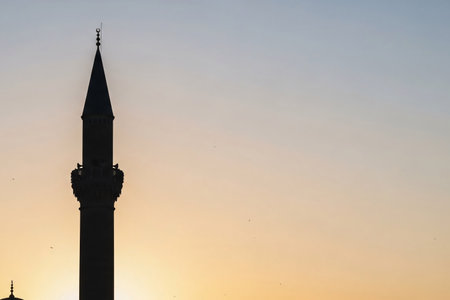 A minimalist photo of an Ottoman minaret silhouette against a soft pastel dawn sky, with a gentle golden glow from the horizon, evoking a peaceful Eid morning.の素材
