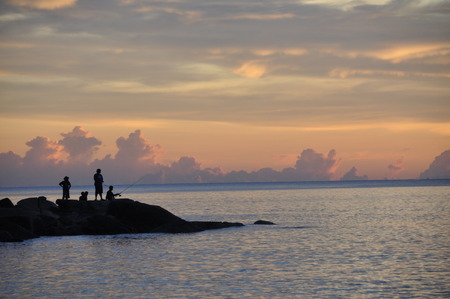 peole are fishing on the rocks near the ocean  at sunsetの写真素材
