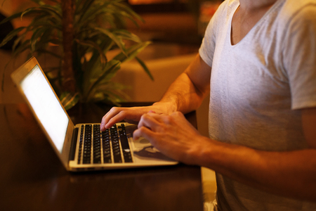 a young handsome man is sitting in a cafe with palm trees with a laptop at sunsetの写真素材