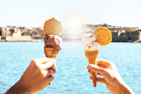 a  couple is holding melting ice cream in waffle  cone under blue sky with bright blue sea on the background in hot summer day on a vacation , holidayの写真素材