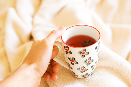 closeup of a man's hand  holding a cup of hot  tea early in the morning in bed after waking up on the blanketの写真素材