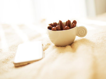 A cup of coffee or tea with chocolate biscuits  is standing on the bed early in the morning with a mobile phone next to itの写真素材