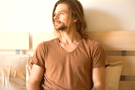 a young serious man  is looking out of the window thinking about something lying in bed after wake...