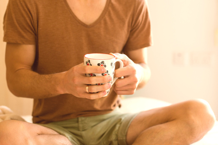 closeup of a young man's hands  holding a cup of tea in the morning in bed after waking upの写真素材