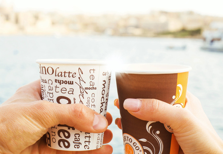 A young couple a man and woman, holding cups of coffee in front of sea and blurred view. Love story conceptの写真素材