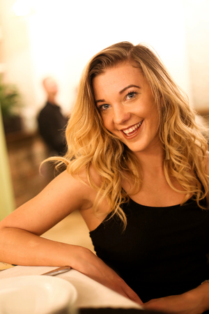 Portrait of a beautiful happy smiling young girl in a black dress,sitting in a restaurant on a date waiting for a dish,laughingの写真素材