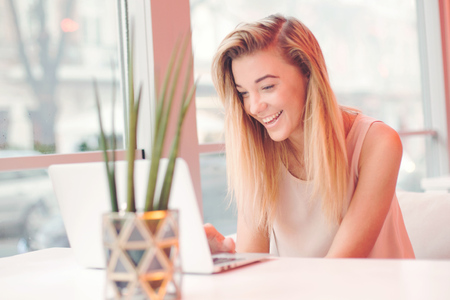 elegant young positive beautiful girl,sitting using laptop computer in a cafe,successful happy business woman,working,looking for information,browsing internet, smiling and looking at you,blurred backgroundの写真素材