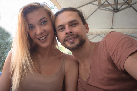 a young beautiful happy couple sitting in a cafe outside and making selfie togetherの写真素材