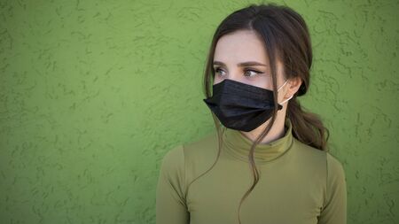 Beautiful girl on the green background with flu medical face mask. Protected and saved from respiratory problems. Facemask dressed.の写真素材