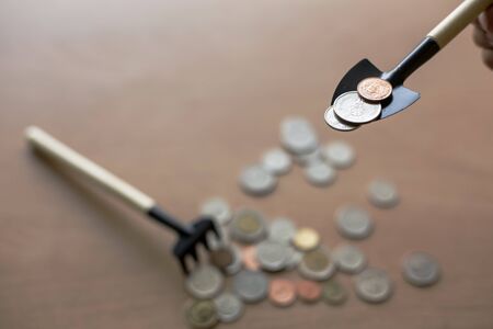 Shovel filled with coins With a pile of coins scattered on the brown floor with a rakeの写真素材
