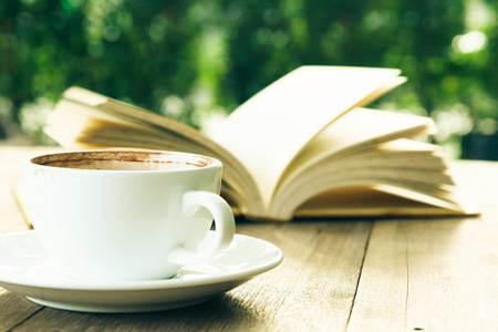 Coffee break and open book on wooden table in gardenの写真素材
