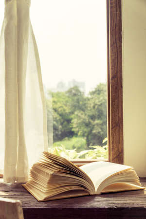 Old book open on wooden desk and window curtain vintage style