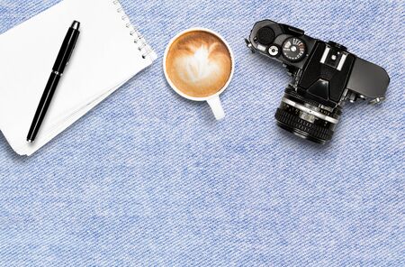 Coffee cup note pad and vintage camera on jean tablecloth background top view flat lay copyspace
