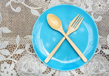 Empty blue ceramic plate wooden spoon and fork on lace tableclothの写真素材