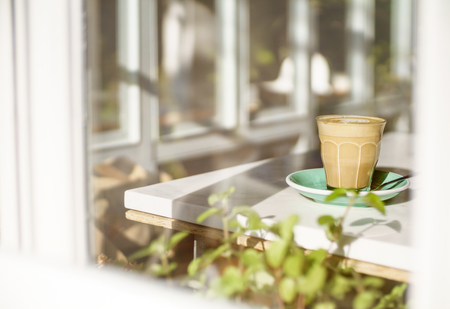 Afternoon hot coffee latte cup beside white glass window shooting from outsideの写真素材