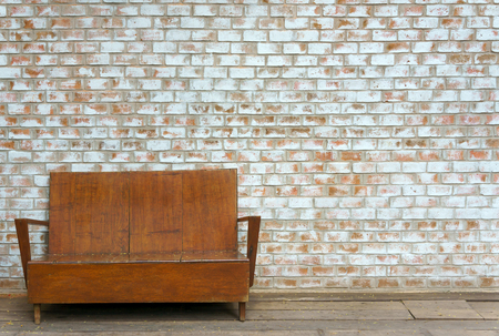 Vintage old outdoor wooden couch on white orange brick wall background textureの写真素材