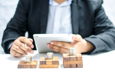 Business and finance concept with stack of coins on wooden table over blurred businessman backgroundの写真素材