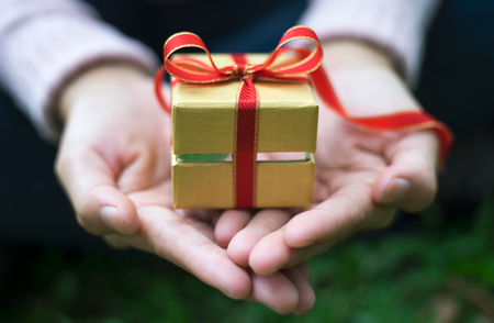 Close up shot of female hands holding a small gift wrapped with red ribbon. Small gift in the hands of a woman outdoor. Shallow depth of field with focus on the little box.の写真素材