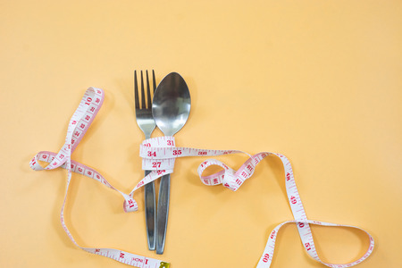 Measuring tape wrapped around fork lying on color surface. Diet concept