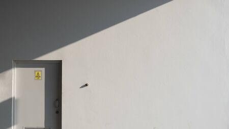 Sunlight and shadow on surface of gray wall and door of electrical control room with yellow warning...