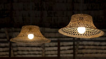 Focus on foreground of 2 vintage hanging lamps decoration with bamboo farmer's hat against straw thatched roof inside of traditional hutの写真素材