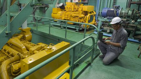 Asian engineer working in engine room. He using laptop in engine inspection of fishing vessel,...