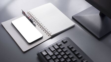 High angle view of smartphone mock up, ballpoint pen, opened spiral notebook, part of computer keyboard and monitor on grey tabletop with sunlight and shadow on surface, selective focusの写真素材
