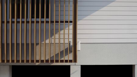 Sunlight and shadow on surface of wooden lath in front of white artificial wood and gray wall with glass window frame of raised covered modern house platform in home architecture conceptの写真素材
