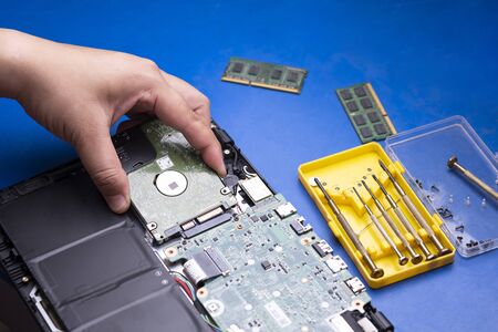 Selective focus at technician hand holding hard disk to install on motherboard of laptop with 2...