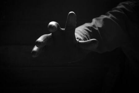 Front view of the scary hand of mysterious criminal in black glove reaching from the dark background in low key style, concept for mystery, crime,danger, threat and horrorの写真素材
