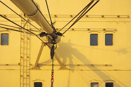Part of the old boom crane with rusty hoist and wire rope sling in yellow nautical ship, vehicle in sea transportation conceptの写真素材