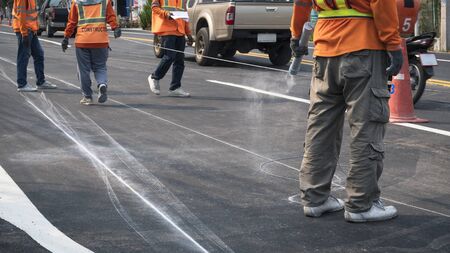 Low section of road workers group are working to marking line for painting traffic color lines on asphalt road while still driving around in the city, focus at man on foregroundの写真素材