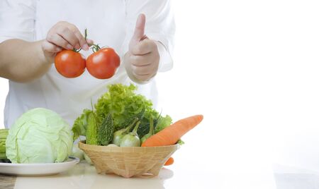 Woman holding fresh tomatoes and showing thumps up with non-toxic vegetables in a bamboo basket on marble tableの写真素材