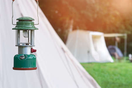 Focus on camping acetylene lantern with blurred background of white tents on camping area in the forestの写真素材