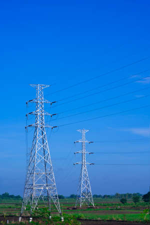 Two high voltage towers and cable lines in countryside with blue sky background in vertical frame
