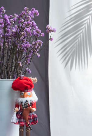 Little red Scottish doll with dried purple statice flowers in white bucket with palm leaf shadow on...