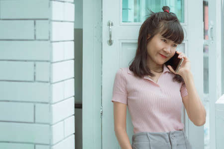 Asian smiling woman talking on smart phone outside of white modern coffee shop
