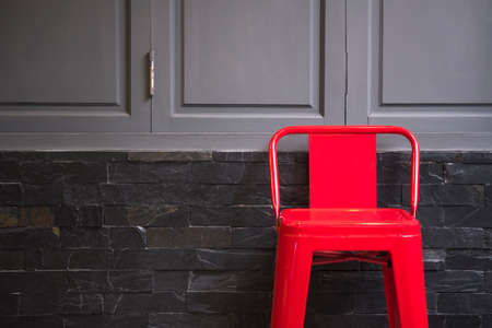 Empty red steel chair in front of grey wooden windows on black slate tiles wall backgroundの写真素材