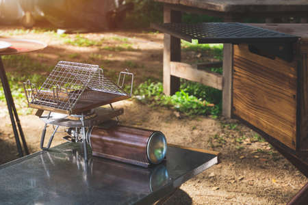Portable gas stove on steel tray and outdoor kitchen table in camping area at morning time