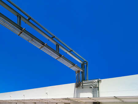 Low angle view of outdoor gas pipelines system into white building against blue clear sky background