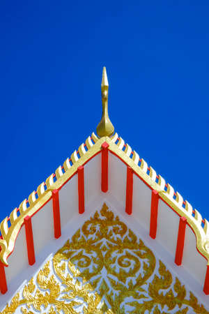 Low angle view of golden gable apex on ornamental Thai temple roof against blue clear sky background...