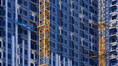 Bangkok, Thailand - August29,2020 : Low angle view of construction workers group on hanging suspended blue platform are working on high-rise building with tower cranes in construction site areaのeditorial素材
