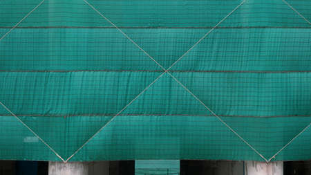 Front view of green mesh sheets covering column of large building in construction site area