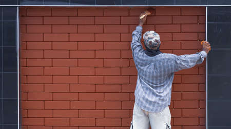 Rear view of Asian worker is painting to renovate the old block in black tile wall border to look...