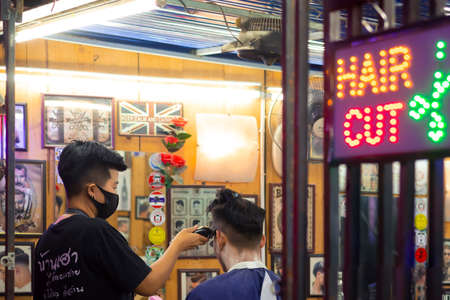 Samutsahhon, Thailand - August 26,2020 : Side view of Asian young female barber stylish in black protective mask is working in street barber shop at outdoor market nightのeditorial素材