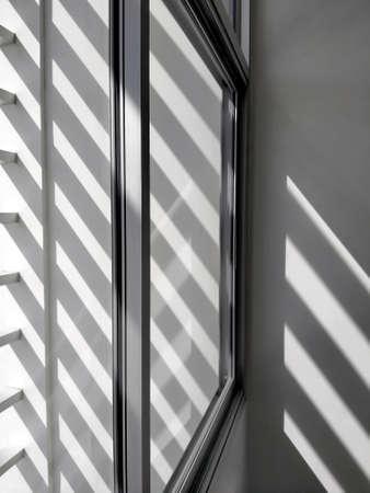 Selective focus at glass window sill, side view and diagonal pattern of sunlight and shadow shining through from outside of building in black and white styleの写真素材
