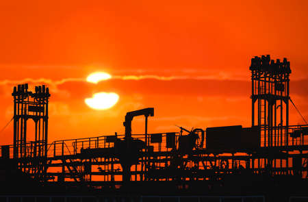 Silhouette pipelines system on crude oil tanker at harbor with blurred sunset sky background
