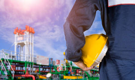 Close up engineer hand in blue mechanic jumpsuit holding yellow safety helmet with blurred...